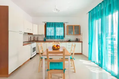 a kitchen with a table and chairs and a kitchen with blue curtains at Cosy House in Kiotari with Garden and Terrace in Kiotari