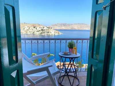 a balcony with a table and chairs and a view of the water at Thodoris Infinity View Apartments in Symi