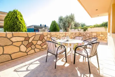 a table and chairs on a patio with a stone wall at Cozy Family Home steps from the Beach in Afantou