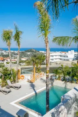 a swimming pool with palm trees and the ocean at Venezia Luxury Living Villas, Faliraki in Faliraki
