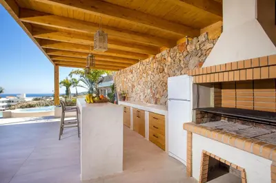 an outdoor kitchen with a stone wall and wooden ceiling at Venezia Luxury Living Villas, Faliraki in Faliraki