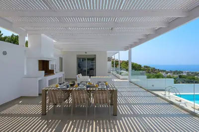 a dining table and chairs on a deck with a view at Villa Allegra with pool in Pefkos, Lindos area in Pefki Rhodes