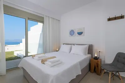 a white bedroom with a large white bed and a chair at Villa Allegra with pool in Pefkos, Lindos area in Pefki Rhodes