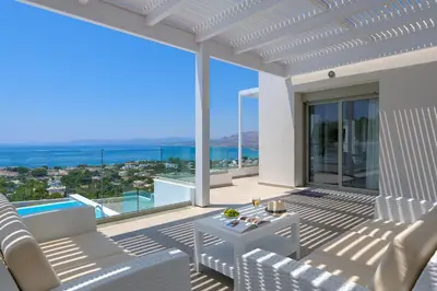 a patio with white chairs and a view of the ocean at Villa Dione in Pefkos, Lindos area in Líndos