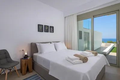 a bedroom with a bed and a chair and a window at Villa Dione in Pefkos, Lindos area in Líndos