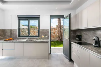 a kitchen with white cabinets and a large window at Villa Summer Dawn in Kiotari