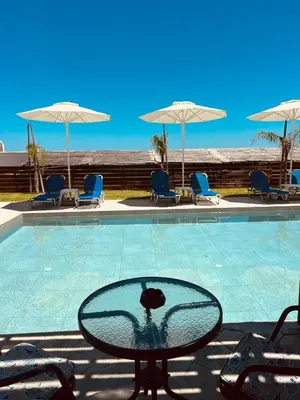 a glass table in front of a swimming pool at Grande Blue Suites with private bay in Archangelos