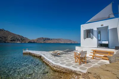 a building with a table and chairs next to the water at On The Rocks in Symi