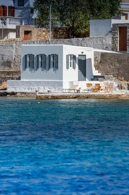a white house with tables and chairs next to the water at On The Rocks in Symi