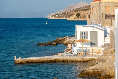 a house on the water with chairs and an umbrella at On The Rocks in Symi