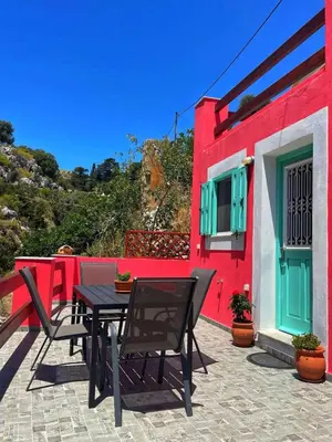 a patio with a table and chairs in front of a red building at Casa Di Rosse in Symi
