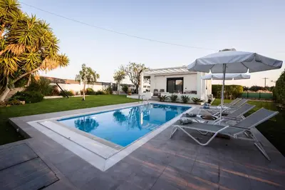 a swimming pool with an umbrella and a chair at El Sueno Villa in Gennadi