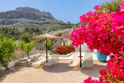 a patio with chairs and umbrellas and pink flowers at Endless Blue Stegna in Archangelos