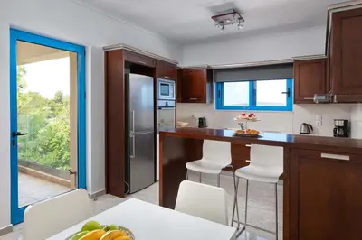 a kitchen with wooden cabinets and a kitchen island with white chairs at Aegean View Estates in Faliraki
