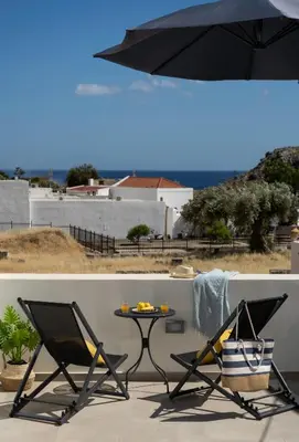 two chairs and a table with an umbrella on a balcony at Lindos Serenity Suites in Líndos