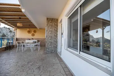 an outdoor patio with a table and chairs and large windows at Aperanto Galazio Apartment in Archangelos