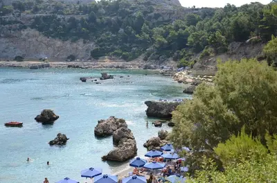 a beach with blue umbrellas and people in the water at Lisabeth Apartments in Faliraki
