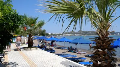 a beach with blue umbrellas and people on the beach at Lisabeth Apartments in Faliraki