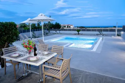 a table with chairs and an umbrella next to a pool at Aegean Horizon apartments in Gennadi