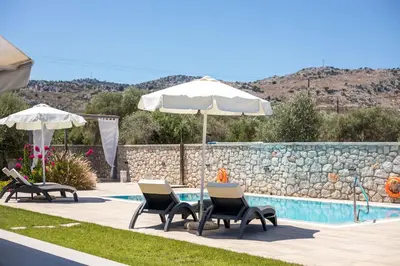 a group of chairs and an umbrella next to a pool at Modern Villa with Pool & Garden Kastalys, Rhodes in Kalithies