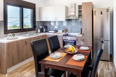 a kitchen with a wooden table with black chairs and a kitchen with a refrigerator at Blue Bay Villas , Ground Floor in Archangelos