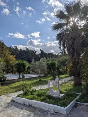 a statue in a park with a palm tree at Artemis Studios - Pool and garden in Koskinou