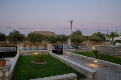 a backyard with a stone fence and grass and lights at Electi Apartments Charaki in Haraki