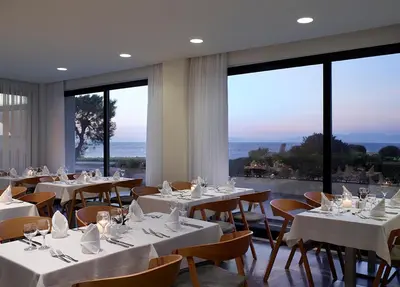 a restaurant with white tables and chairs and large windows at Cactus Hotel in Rhodes Town