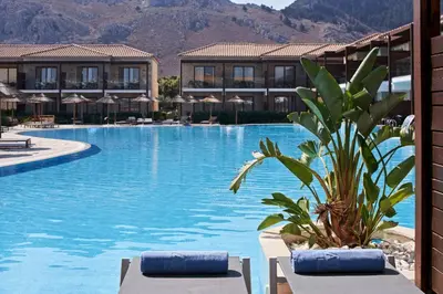 a swimming pool with a resort with mountains in the background at Atlantica Holiday Village Rhodes in Kolimbia