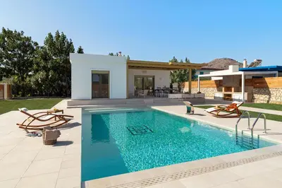 a swimming pool with two chairs and a house at Serenity Villas in Kolimbia