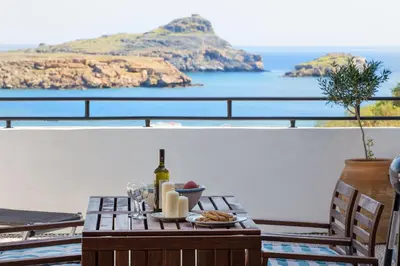 a table with food and a bottle of wine on a balcony at Villa Thalassa 2 Cozy Greek Comfort Private Shaded Courtyard in Líndos
