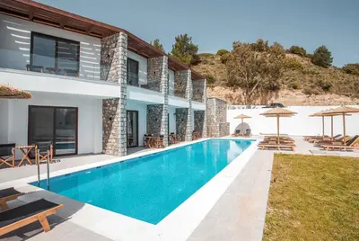 a swimming pool in front of a house with umbrellas at Terra Pietra Luxury Villas & Suites in Lardos