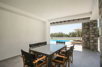 a dining room with a table and chairs and a swimming pool at Terra Pietra Luxury Villas & Suites in Lardos