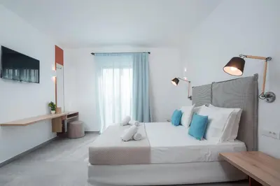 a white bedroom with a large bed with blue pillows at Terra Pietra Luxury Villas & Suites in Lardos