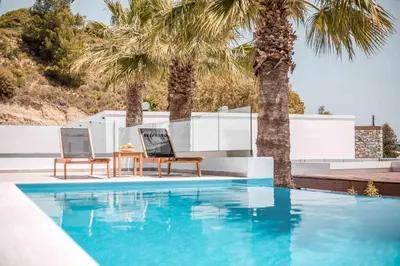 a swimming pool with two chairs and a table next to palm trees at Terra Pietra Luxury Villas & Suites in Lardos