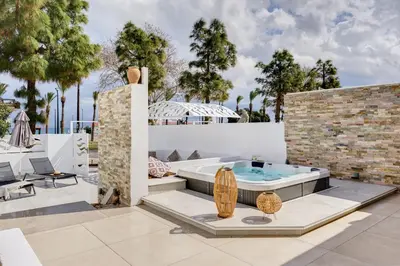 a patio with a hot tub and chairs and trees at Sia Mare Seaside Apartments in Faliraki