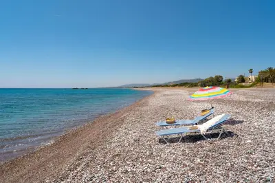 two lounge chairs and an umbrella on a beach at Tselios Apartments & Studios in Kiotari