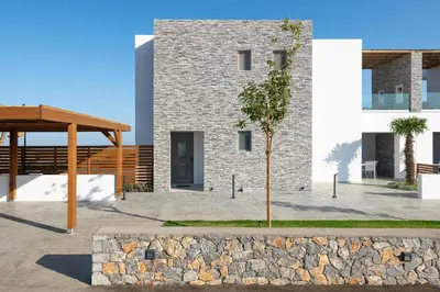 a building with a stone wall and a tree at Anemos Villas in Lachania
