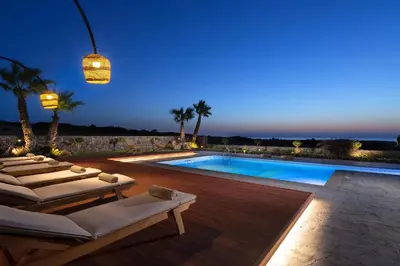 a villa with a swimming pool at night at Anemos Villas in Lachania