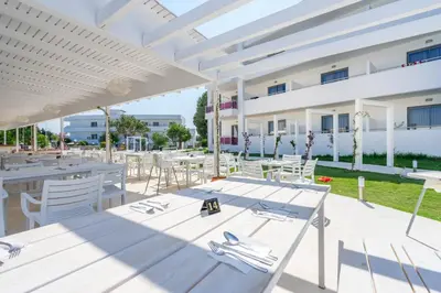 a patio with white tables and chairs and a building at Stamos All Inclusive in Faliraki