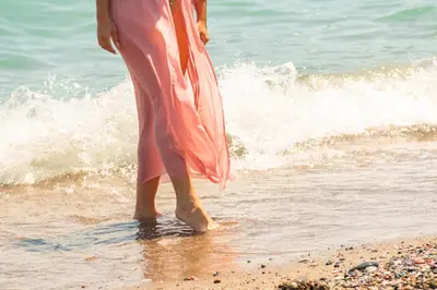 a woman in a pink dress standing on the beach at Sun Beach Lindos in Lardos