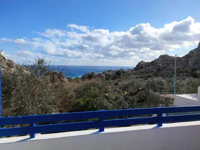 a blue bench on a road looking at the ocean at Ioli's Apartments in Archangelos