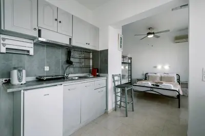 a kitchen with white cabinets and a bed in the background at Mike's Studios in Haraki