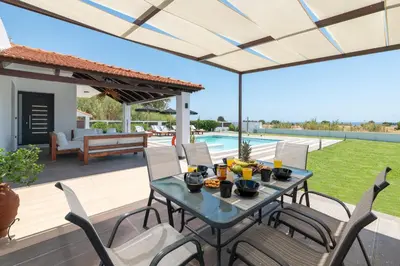 a patio with a table and chairs and a pool at Elysian Villa in Afantou