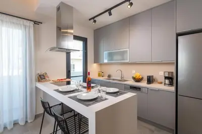 a kitchen with white cabinets and a large island with chairs at Lucian City Apartments in Rhodes Town