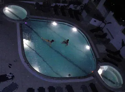 two people swimming in a swimming pool at night at White Palace Pavlos apartment1 in Faliraki