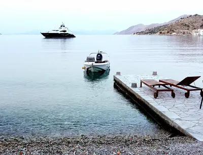 a boat in the water next to a table and a bench at Symi . VILLA CALME (Sur la Mer). in Symi