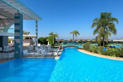 a pool at a resort with white chairs and a bridge at Oceanis Beach Hotel in Ixia