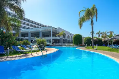 a large swimming pool with palm trees and a building at Oceanis Beach Hotel in Ixia