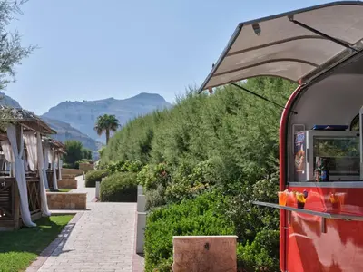 a food cart with an umbrella next to a sidewalk at Atlantica Aegean Park in Kolimbia